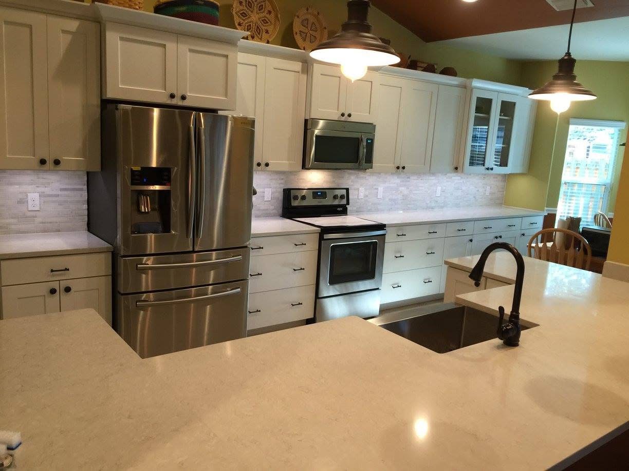 Finished kitchen with white shaker cabinets, marble mosaic backsplash and quartz island