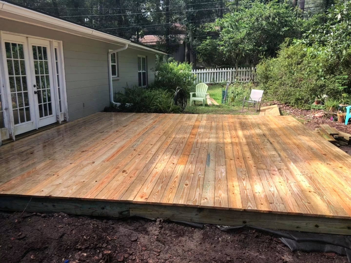 Deck build step 4 of 4: completed backyard deck installed flush against the back of the house after a light rain, showing the full finished project