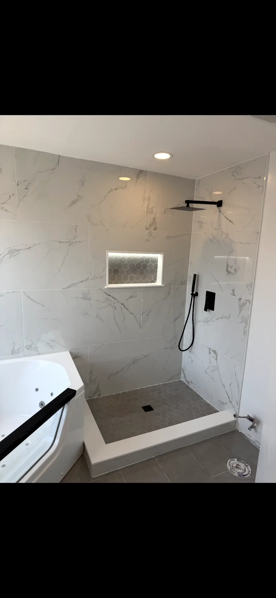 Marble-look tile shower with black rain head and lit hex niche